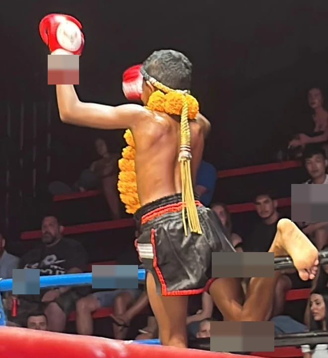 A young boxer seen from behind in a Muay Thai ring.